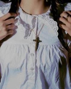 a woman wearing a white shirt with a cross on the chest and necklace around her neck