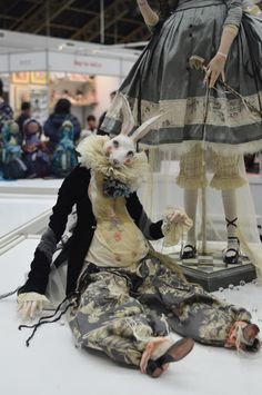 two mannequins dressed in costumes on display at an art fair, one is sitting down and the other is standing up