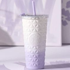 a starbucks cup with a purple straw in it on a table next to a wall