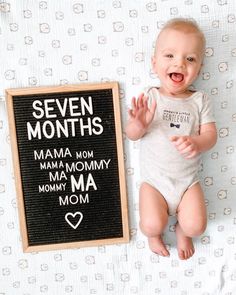 a baby laying on top of a bed next to a sign that says seven months