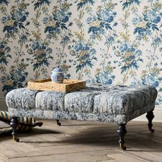 an upholstered bench in front of a floral wallpapered room with wooden flooring