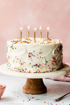 a birthday cake with white frosting and sprinkles on a wooden stand