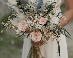 a woman in a white dress holding a bouquet of flowers and greenery on her wedding day