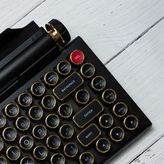 a black and gold typewriter sitting on top of a white wooden table next to a pen