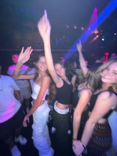 a group of young people dancing at a club or party with their arms in the air