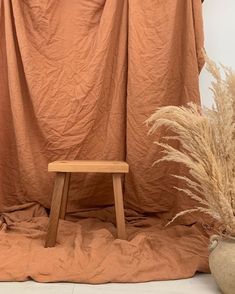 a wooden stool sitting in front of a drape covered wall next to a potted plant