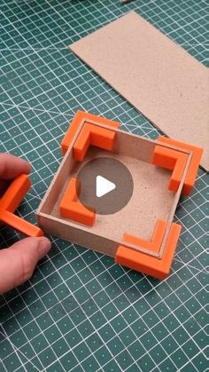 someone is making an object out of cardboard and orange plastic blocks on a table with scissors