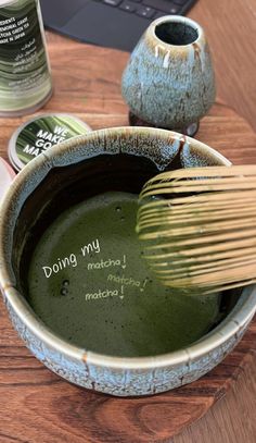 a wooden table topped with a bowl filled with green liquid and a whisk