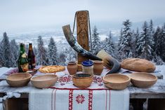 a table topped with wooden bowls filled with food next to snow covered mountains and trees