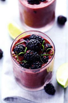 two glasses filled with berries and limes on top of a white cloth next to lemon wedges