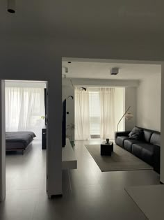 an open living room and bedroom area with white walls, black leather couches and large windows