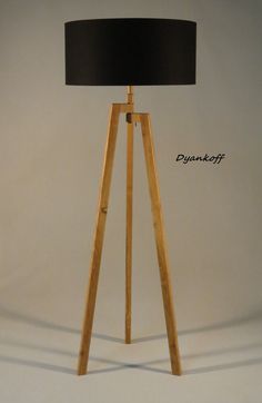 a wooden tripod floor lamp with a white shade on the top and bottom half