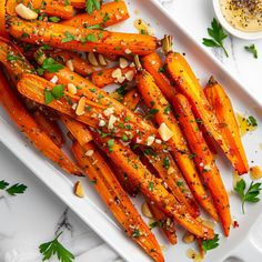 roasted carrots with herbs and seasoning on a white platter next to a small bowl of dipping sauce