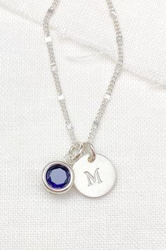 For her birthday, show her lots of love by gifting her a personalized piece of jewelry that she can treasure and wear daily. Her September birthstone, a sparkling lab-created blue sapphire, is back-set in sterling silver. This lovely centerpiece is complemented by a hand-stamped initial charm disc, customized with the letter of your choice.  These captivating charms dangle from a delicate, shimmering chain that fastens with a spring ring clasp. All elements of this stunning piece are meticulousl Silver Necklace For May Birthstone Birthday, Elegant Engraved Charm Necklaces For Birthday, Personalized Silver Birthstone Necklace For Birthday, Silver Birthday Necklaces With May Birthstone, Personalized Silver Birthstone Necklace For Birthday Gift, Birthday Birthstone Necklace With Round Stone, Silver Necklace With May Birthstone, Silver Necklace With May Birthstone For Birthday, Silver Necklace For Birthday With May Birthstone