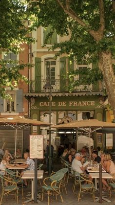 people sitting at tables under umbrellas in front of a building on a city street