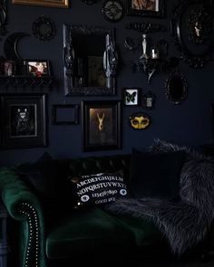 a living room with black walls and pictures on the wall, green velvet couch in foreground