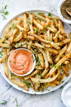 french fries with ketchup and herbs on a white plate next to some dipping sauce