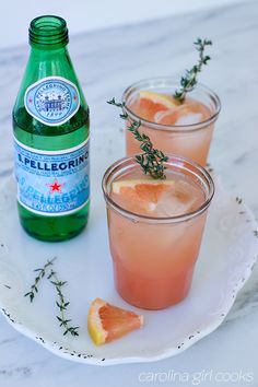 two glasses filled with pink lemonade and garnished with herbs on a plate next to a bottle of water