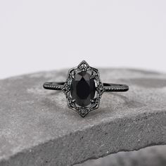 a black diamond engagement ring sitting on top of a stone slab in front of a white background