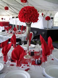 a white table topped with red napkins next to a tall vase filled with flowers