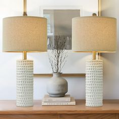 two white vases sitting on top of a wooden table next to a wall mounted mirror