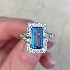 A captivating aquamarine engagement ring that centers a 1.55 carat emerald cut aquamarine gemstone. The aquamarine is Santa Maria color, with a strong blue saturation and a clean crystal. Santa Maria is the best possible color for aquamarines. Surrounding the gemstone is a row of diamonds. Two sections of diamonds adorn the shoulders.
This platinum ring features delicate open-work along the under-gallery. The approximate total diamond weight of this ring is 0.35 carats.
The measurements of the c Blue Art Deco Jewelry Gia Certified, Gia Certified Blue Art Deco Jewelry, Luxury Blue Baguette Cut Topaz Ring, Emerald-cut Topaz Ring In 14k White Gold, Blue Topaz Ring With Square Cut, 14k White Gold Emerald-cut Topaz Ring, Elegant Blue Baguette Cut Topaz Ring, Blue Baguette Cut Topaz Ring, Classic Emerald Cut Blue Topaz Jewelry