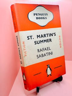 an orange and white penguin book sitting on top of a pink table next to a wall