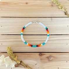 a bracelet with multicolored beads sits on a wooden table next to a flower