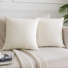 two white pillows sitting on top of a couch next to a cup and saucer