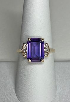 This vintage ring is very "pre-loved". The center stone is in good shape for the age. I've not formally tested it. It is doubly refractive with sharp facet junctions, resembling a lab-grown sapphire, however there is no color change, like some. It is reminiscent of fine African amethyst. The sides there is damage to prongs. I've tried to polish this up a bit. All the diamonds are natural and one of them is a bit smaller and has a very worn down prong. Still, all stones are tight. Item is being s Collectible 14k Gold Birthstone Ring With Gemstone, Vintage Amethyst Ring With Center Stone For Promise, Vintage Amethyst Ring With Accent Stones For Promise, Collectible 14k Gold Birthstone Ring, Collectible Birthstone Ring In 14k Gold, Heirloom 14k Gold Amethyst Ring With Accent Stones, Vintage Emerald Cut Amethyst Ring For Anniversary, Antique Anniversary Ring With Accent Stones, Antique Anniversary Rings With Accent Stones