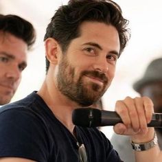 a man with a beard holding a microphone in his right hand and smiling at the camera