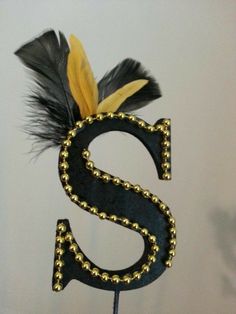 the letter s is decorated with black feathers and gold beadings on a metal stand