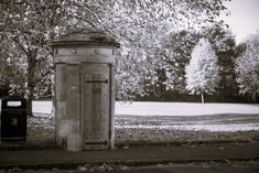 an old phone booth sitting in the middle of a park next to a trash can