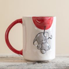 a red and white coffee mug with an elephant on it's side sitting on a wooden table