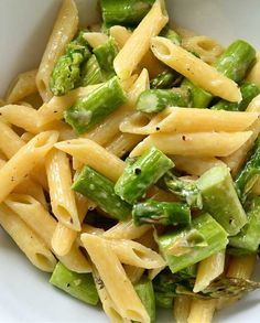 a white bowl filled with pasta and asparagus on top of a wooden table