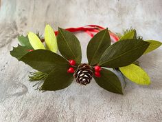 a pine cone and green leaves with red berries are on the headband for this christmas wreath