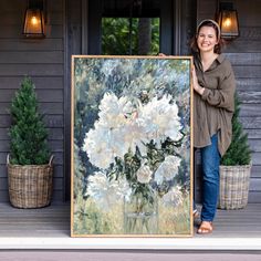 a woman standing in front of a painting holding a vase with white flowers on it