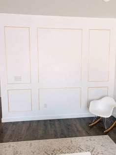 a white rocking chair sitting in front of a wall with gold lines painted on it