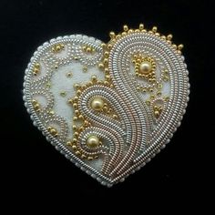 two white and gold heart shaped brooches on a black background, with beads in the center