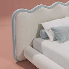 a white bed with blue and gray pillows on it's headboard, against a pink background