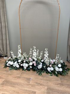 an arrangement of white flowers and greenery in front of a gold frame on the floor