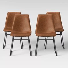 three brown leather chairs sitting next to each other on top of a white surface with black metal legs