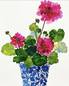 a blue and white vase filled with pink flowers on top of a green leafy plant