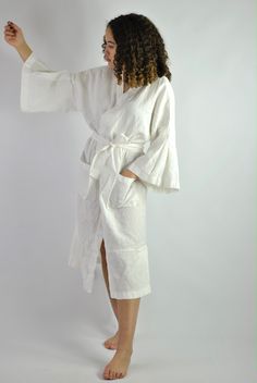 "This is our no. 60 of Conscious Clothing Concept #stayhome This lovely white A-line loose fitting robe is made of pure quality linen. Very modern approach to traditional white spa gown. It has got very flattering wide sleeves that match the bottom of the dress. This unique piece of loungewear can be very versatile. It is great and comfy to wear around the house, hotel or spa. It can be treated as the dress or loose shirt over the shorts for summer look. Perfect for home and the beach. It is the White Spring Kimono For Relaxation, White Kimono For Brunch In Summer, White Wrap Robe For Vacation, White Wrap Dress For Daywear, White Wrap Day Dress, White Long Kimono For Loungewear, White Kimono With Kimono Sleeves For Brunch, White Spring Robe For Relaxation, White Kimono For Brunch