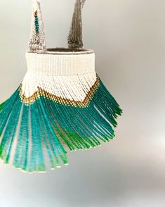 a green and white beaded purse hanging from a hook on a gray background,