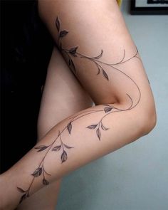 a woman's legs with tattoos on them, and one leg has leaves growing out of it