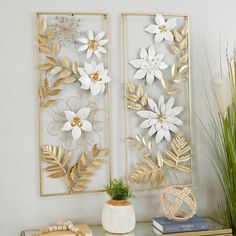 two gold and white metal wall art pieces on a shelf next to a potted plant