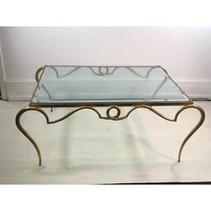 a glass top coffee table with gold metal frame and scroll design on the bottom, sitting against a white wall