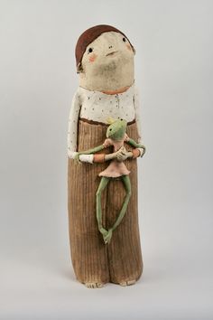 a wooden statue with a frog on it's back and a person holding an object in its arms