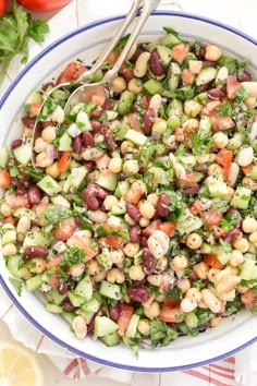 a bowl filled with beans, cucumber and parsley next to lemon wedges